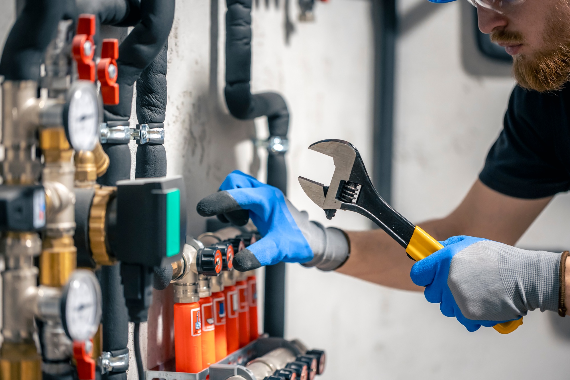 A man installs a heating system in a house and checks the pipes with a wrench.
